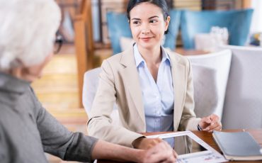 Insurance agent at work Young businesswoman sitting at the table with touchpad and communicating with senior woman